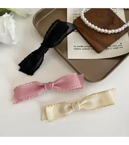 Detailed view of elegant bow hair clips in black, pink and beige with wavy ribbon texture