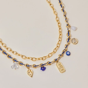 Detail of layered gold chain necklace with blue woven cord and evil eye charms