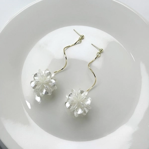 Close-up of elegant white shell flower earrings with golden metal waves on a white plate