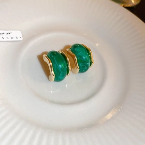 Close-up of vintage emerald green resin earrings with gold plating on ceramic tray