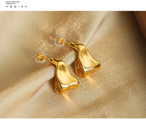 Detailed view of gold plated geometric wave earrings resting on elegant champagne silk fabric