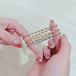 Detail view of 18K gold and silver elastic beaded bracelets held by hands