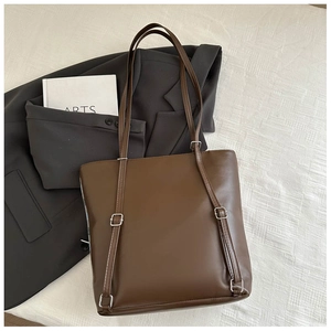 Detail of a brown leather tote bag with silver hardware placed on a grey blazer suit