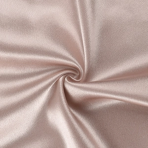 Détail du tissu satiné or rose montrant une texture élégante et des plis en spirale