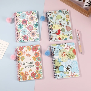 Vista de cuadernos de espiral con pompones de felpa y portadas de flores de dibujos
