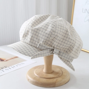 Detailed close-up of a plaid beret with a bow on a wooden stand in a vintage scene