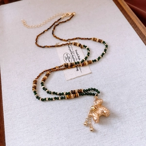 Détail du collier de perles avec perles vertes facettées et un pendentif chiot doré