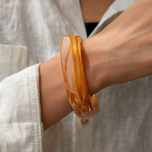Detail of amber acrylic bracelet with white swirl pattern worn on woman wrist