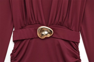 Close-up detail of wine red dress waist with elegant draped folds and gold metallic buckle