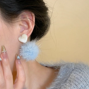 Elegant fabric heart and light blue pompom drop earrings worn by a model on plain background