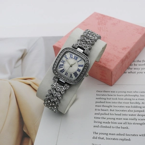 Close-up of silver square watch with blue Roman numerals and pavé crystal rhinestones