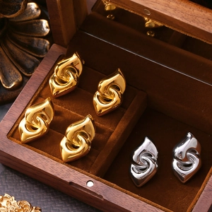 Golden and silver heart-shaped twisted steel earrings on a wooden jewelry box