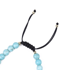 Macro shot of turquoise beaded bracelet featuring black braided rope and gold beads