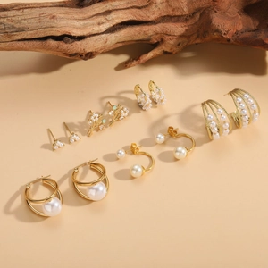 Detailed set of golden pearl earrings with zircon flowers on a rustic wooden backdrop