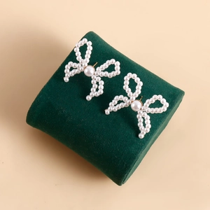 Detail of handmade bow knot faux pearl earrings on a green velvet display stand