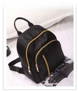 Detail of black nylon backpack with three front gold zipper pockets and a leather handle