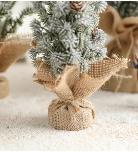 Close-up of mini snow-flocked Christmas tree with natural pine cones and burlap base