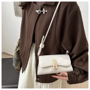 Close-up of a white textured leather underarm bag featuring a gold buckle on a brown wool coat