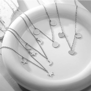 Detailed view of stainless steel necklaces with heart, moon, and star charms in a ceramic bowl