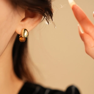 Close-up of golden metal earrings with brown faux tiger eye stone on model's ear