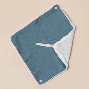 Detail of baby muslin bib showing grey-blue cotton fabric, pom-pom trim and snap closure