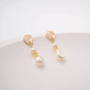 Elegant baroque pearl drop earrings with geometric gold metal on white minimalist surface