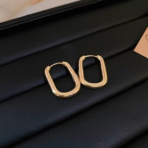 Detailed close-up of polished gold rectangular earrings on black leather surface
