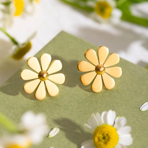 Detail view of 18k gold stainless steel daisy earrings on a green textured surface