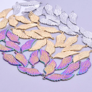 Set of stainless steel wing pendants in gold, silver, and rainbow finishes on purple background