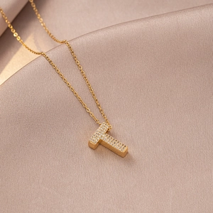 Detailed close-up of golden T-letter pendant necklace with micro-paved zircons on silk