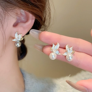 Detail of butterfly pearl earrings with gold base and white wings worn by a model