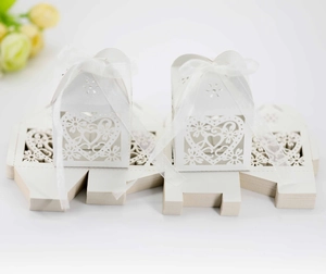 Detail of white laser-cut wedding favor box with heart patterns and satin ribbons