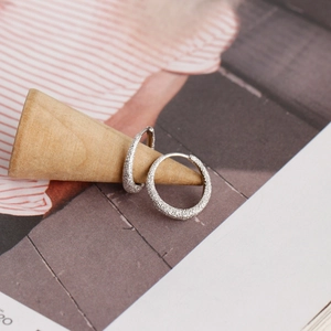 Close-up of silver hoop earrings with sparkling sand surface on a wooden cone stand
