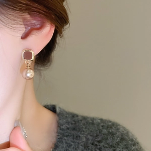 Detailed view of vintage gold square enamel earring with a round pearl drop on model