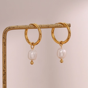 Close-up of 18K gold-plated hoop earrings with baroque pearls on a vintage stand