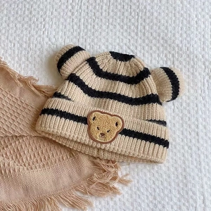 Gros plan d'un bonnet tricoté beige rayé avec oreilles d'ours 3D et patch brodé