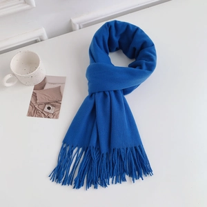 Detail shot of a blue knitted scarf with tassels neatly folded on a white surface