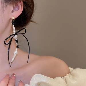 Detailed view of long bowknot earring with pearls and black beads on a female model