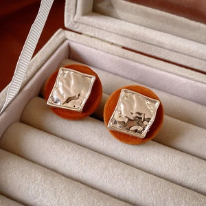 Macro shot of silver irregular square metal studs with orange velvet backing in a beige box