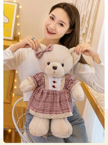 Detail of teddy bear plush in red checkered dress held in hands by a smiling woman