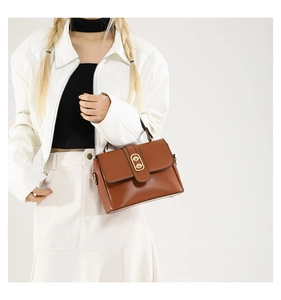Detailed close-up of a caramel brown leather handbag featuring a gold oval double-ring lock