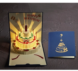 Illuminated 3D pop-up birthday card featuring a glowing three-tier cake and warm lights