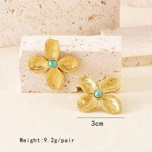 Vintage gold clover earrings with turquoise beads set on a textured stone background