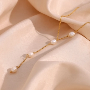 Detailed close-up of golden stainless steel Y-chain with pearls on champagne silk fabric