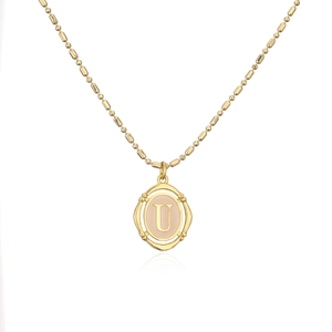 Detalle del colgante ovalado dorado con textura de bambú y letra U en cadena de bolas