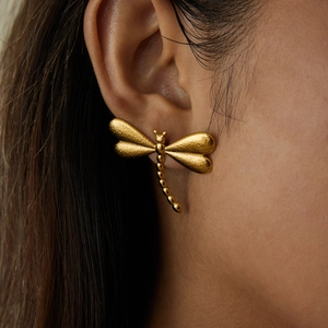 Élégantes boucles d'oreilles libellule dorées en acier titane mat sur un modèle
