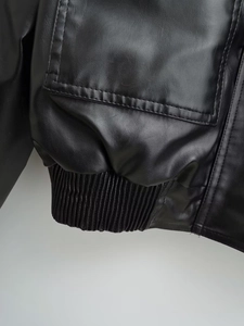 Detail of black faux leather jacket showing ribbed elastic hem and cuff stitching