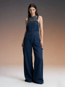 Détail d'une salopette en jean bleu foncé avec boucles métalliques et coutures de poche