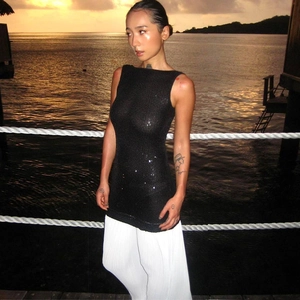 Detail view of a sequin sleeveless top paired with pleated white trousers in a sunset scene