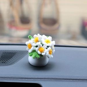 Handmade pipe cleaner daisy in white pot on car dashboard with blurred background